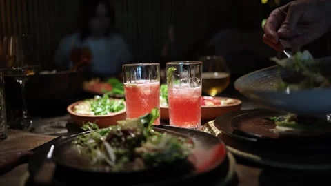 People share and cut steak at a lively dinner table with assorted dishes Stock Footage 344744819