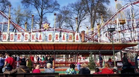 People sit on benches in front of roller-coaster in funfair Stock Footage 62175995