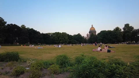 People sit on the grass in the park in front of St. Isaac's Cathedral in the eve Видео 157155135