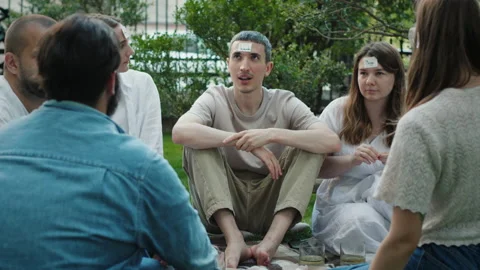 People sit on ground in yard playing guessing game at break Stock Footage 219953169