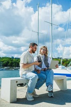 People sit at a harbor discussing work while holding a laptop and a coffee .. Stock Photos