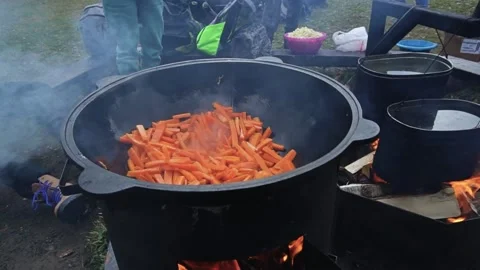 People sit near the fire while food is being cooked in the cauldrons. Carrots Video stock 169786237