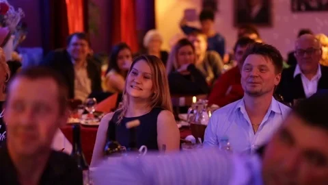 People sit at tables, watch a performance in a restaurant and laugh. Видео 80941604