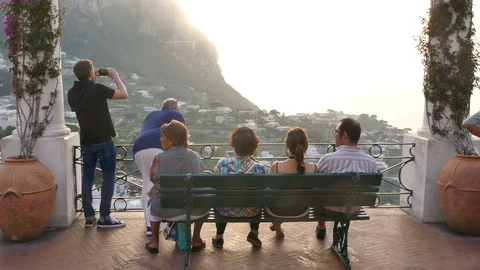 People sitting on a bench at a viewpoint looking at the island of Capri sunlight Stock Footage 112345082