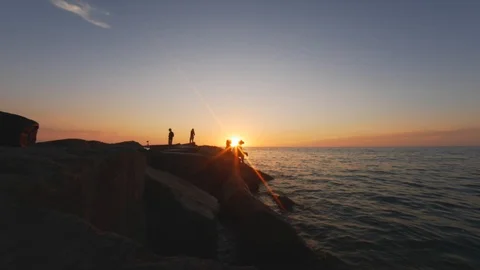 People sitting in Front of Sun while Sun is Setting over Ocean Stock Footage 104891042