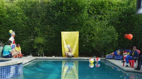 People sitting at the pool side looking at the man with bag over his head Stock Footage 108943664
