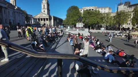 People sitting on the steps at Trafalgar Square enjoying sunlit urban life and Видео 334294931