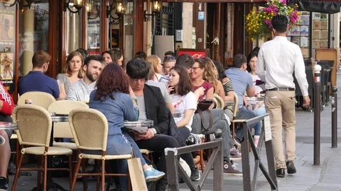People sitting at street restaurant cafe tables in city center of Paris Stock Footage