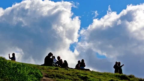 People sitting on top of a hill as clouds pass by. Видео 135859199