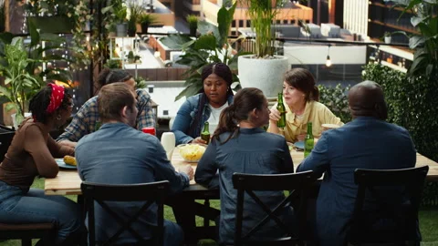 People socializing around rooftop dining table with food and bottled drinks Stock Footage 347067074