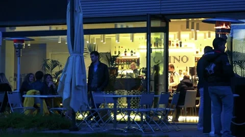 People stand and sit in front of restaurant at evening  Stock Footage 65997762