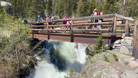 People standing on a bridge over a waterfall in the Grand Teton mountain range. Stock Footage 320260290