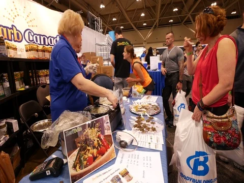 People stop by a vendor booth to check out their food in a public consumer show Stock Footage 76503077
