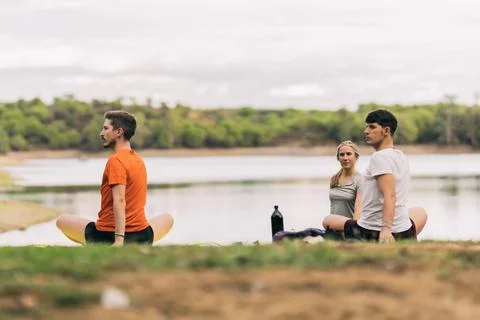 People stretching while doing yoga in a park next to a lake Stock Photos