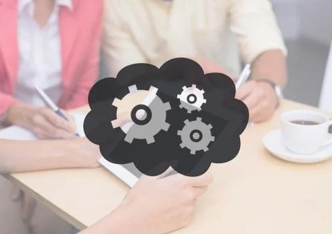 People at table with tablet behind grey cloud and gear graphic Stock Photos