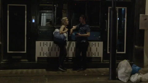 People Talking Outside a Closed Storefront on City Street at Night Stock Footage 344624216
