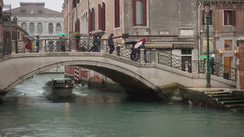 People with umbrellas crossing bridge while police boat passes in Venice Stock Footage 325316449