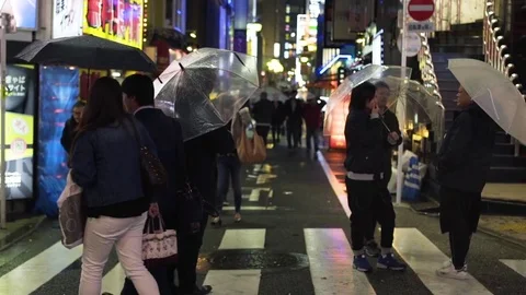 People with umbrellas walking along street on rainy night Stock Footage 79444053