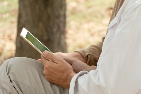 People using digital tablet sitting on bench in the park Stock Photos