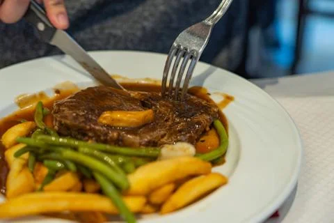 People using knife and fork eating beefsteak and french fries Foto stock