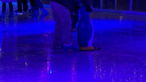 People using penguin skating aids on a glowing blue indoor ice rink, captur.. Stock Footage 340882071