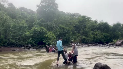People wading through a flowing river in a forest, holding hands for support Stock Footage 340252557