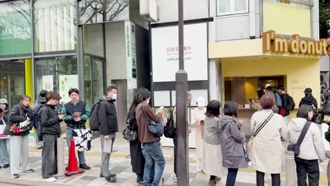 People Waiting in a Long Queue Outside a Yellow Donut Shop in Tokyo Stock Footage 331898349