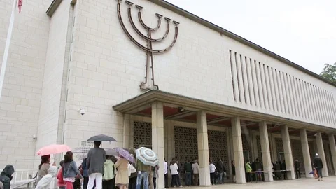 People waiting in queue to enter the Synagogue on a rainy day Stock Footage 85125608