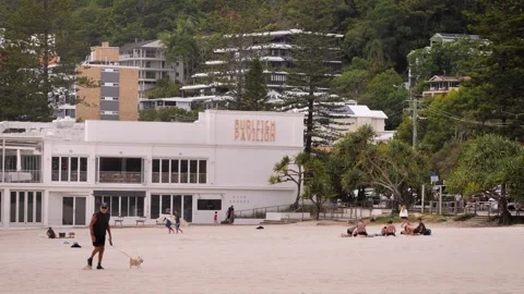 People walk across the beach in front of the Burleigh Pavilion on an overcast Stock Footage 346918730