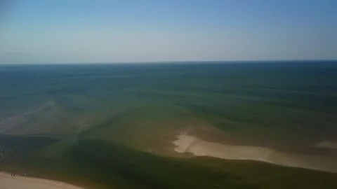 People walk along a long beach with clear water on a sunny day in a coastal.. Stock Footage 339938548
