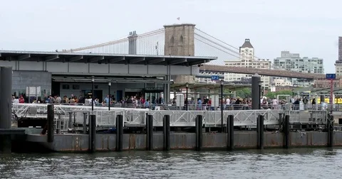 People walk and wait in line on Pier 11 while boats pass by on the East River Stock Footage 77519684