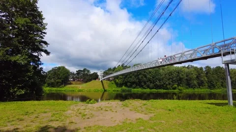 People walk on a bridge above a river surrounded by trees in a park on a sunny d Vídeos de archivo 340448325