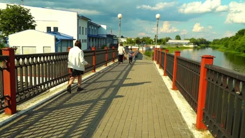 People walk on a bridge by a river in a town under a blue sky with clouds in the Stock Footage 340448037