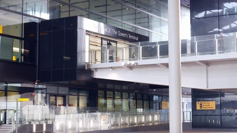 People walk on elevanted walkaway leading to modern glass entrance at Heathrow Stock Footage 103146664