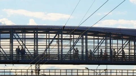 People walk over elevated glassy bridge in silhouette on a bright day 4K. Stock Footage 114276579