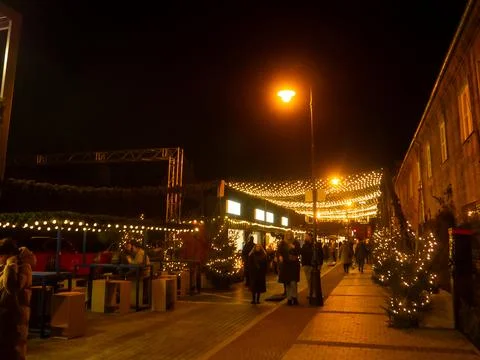 People walk under string lights on a street in the evening during a festive time Foto stock