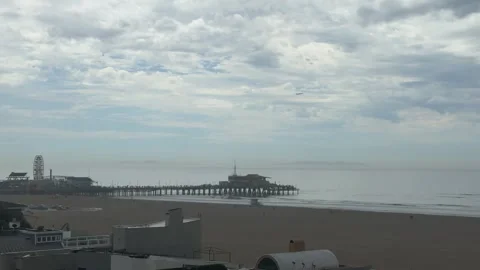 People walking along a beach with a pier under overcast skies in Santa Monica Stock Footage 345266053