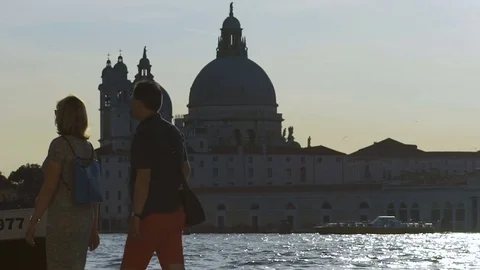 People walking along waterfront, speedboat passing by church across river Stock Footage