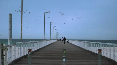 People walking down pier on white sand beach with blue sky Stock Footage 99292246