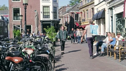 People walking down urban street in sunshine with parked bicycles and cafe Stock Footage 169098053