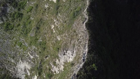People Walking on Edge of Steep Cliff next to Beautiful Beach [Drone Footage] Stock Footage 96285754