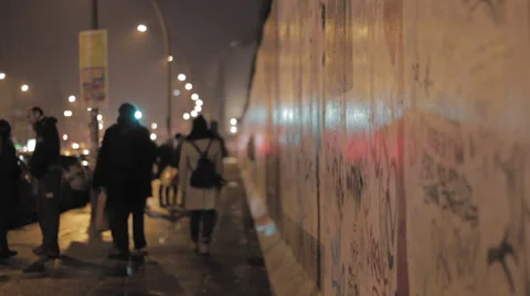 People walking next to Berlin wall at night, car lights casting shadows Stock Footage 67986435