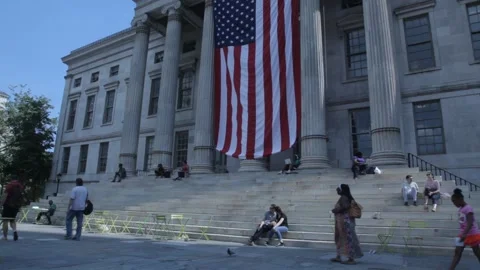 People Walking Past Large US Flag on Historic Building 動画素材 341324404