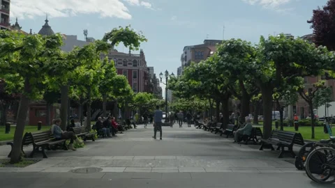 People Walking Through Tree-Lined Promenade at Plaza San Miguel, Gijón Видео 334824988