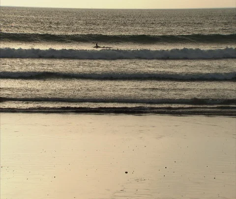 People walking in wet sand with waves washing up on shore behind Stock Footage 86747189