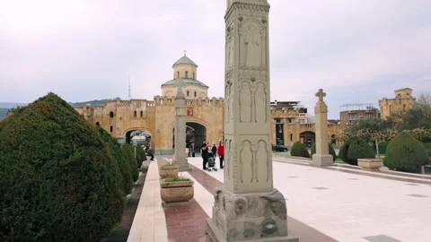 People walking within Holy Trinity Cathedral complex, passing a carved stone Stock Footage 334613781