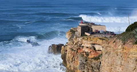 People watching the big giant waves crashing near the Fort of Nazare Stock Footage 221582066