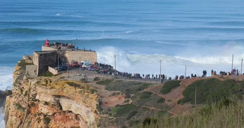 People watching the big giant waves crashing near the Fort of Nazare Stock Footage 221582543