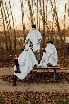 People wearing ghost sheets sitting on park bench Stock Photos