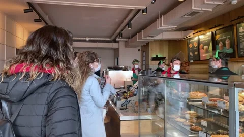 People wearing medical masks standing in line Starbucks ordering coffee Stock Footage